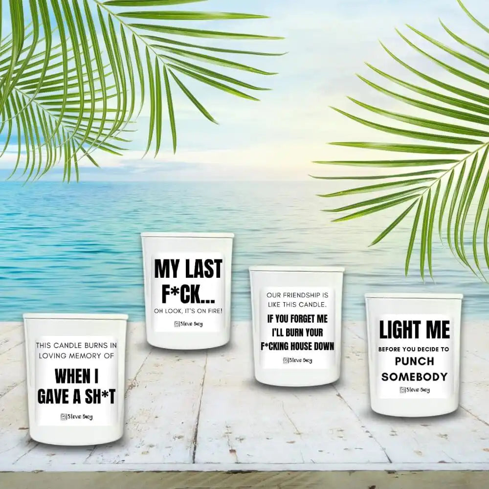 Four white candles with humorous profanity-themed messages printed on them.